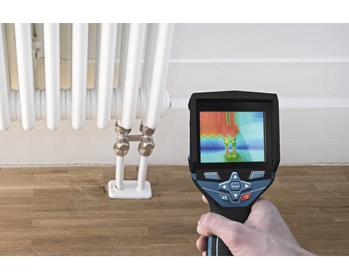 Une main tient une caméra thermique devant un radiateur pour mesurer la température.