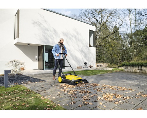 Un homme balaie les feuilles avec une balayeuse devant une maison.