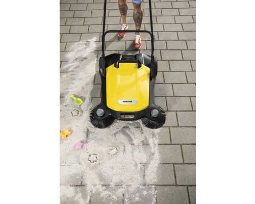 Balayeuse jaune en action sur des pavés avec du sable et des jouets d''enfants.