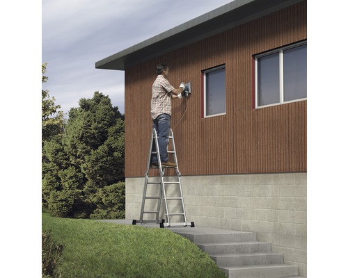 Un homme travaille avec une ponceuse sur une échelle devant une maison.