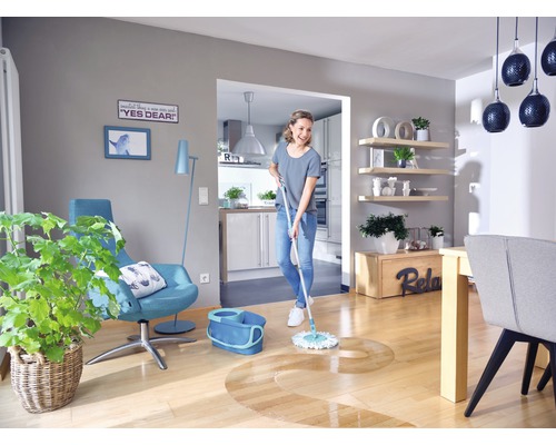 Frau wischt Holzboden im hellen Wohnzimmer mit Wischmopp