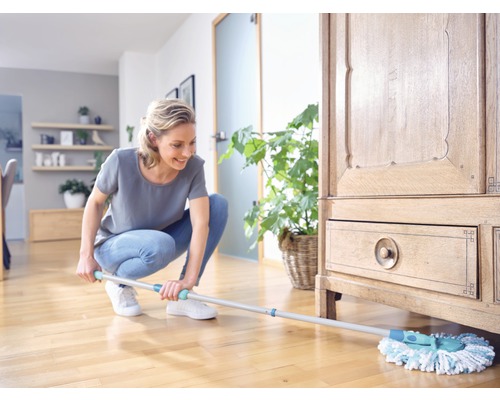 Frau wischt Holzboden im Wohnzimmer mit Wischmopp