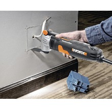Une main utilise un outil multifonction Worx pour découper une ouverture dans une paroi métallique.