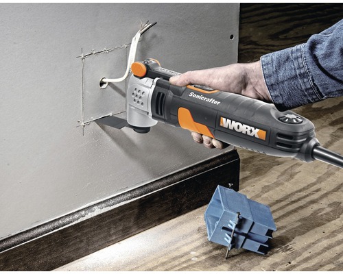 Une main utilise un outil multifonction Worx pour découper une ouverture dans une paroi métallique.