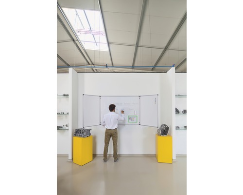 Un homme écrit sur un tableau blanc en trois parties dans une pièce avec des expositions