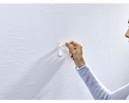 Frau befestigt einen Klebehaken an einer Wand