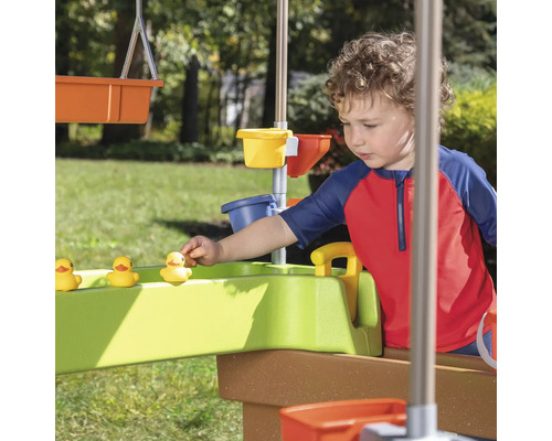 Kind spielt mit Wasserspieltisch und gelben Enten im Garten.