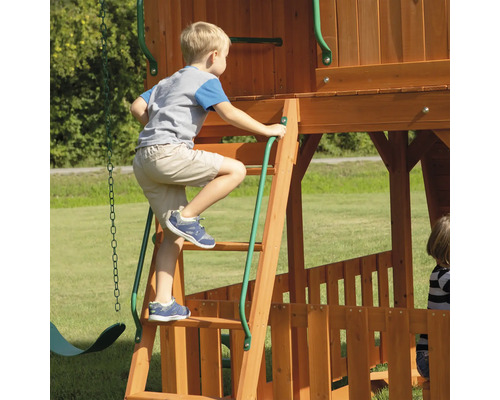 Un enfant grimpe sur une aire de jeux en bois avec une échelle.