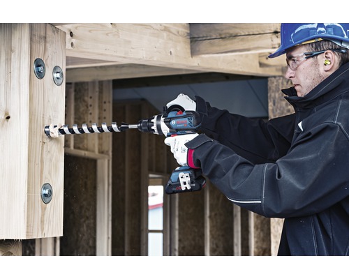 Ein Mann bohrt mit einem Akku-Bohrschrauber ein Loch in einen Holzbalken.