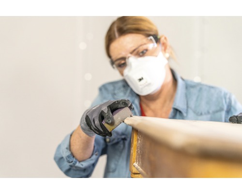 Femme ponçant du bois avec du papier de verre, des lunettes de protection et un masque respiratoire