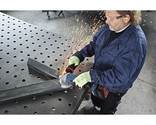 Un homme meule du métal avec une meuleuse d'angle sur une table de travail.