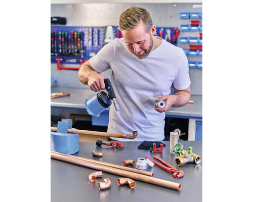 Un homme soude des tuyaux de cuivre avec un chalumeau et de l''étain sur un établi.