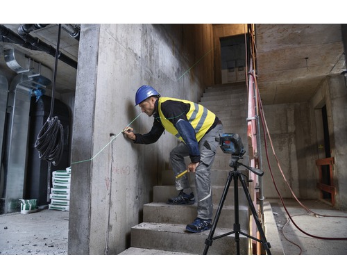 Un ouvrier du bâtiment utilise un laser linéaire sur un chantier pour marquer une ligne droite sur un mur en béton.