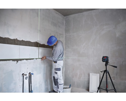 Un homme pose des carreaux avec un laser linéaire dans une pièce.