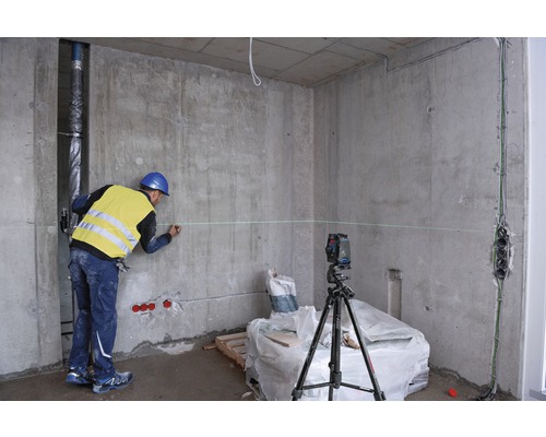 Ouvrier du bâtiment marquant un mur avec un niveau laser dans un bâtiment brut