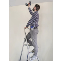 Handwerker auf einer Leiter, der mit einem Akkuschrauber an einer Decke arbeitet