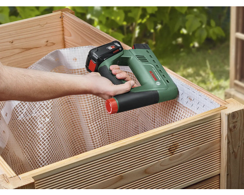 Eine Person befestigt mit einem Akku-Tacker Vlies in einem Hochbeet.