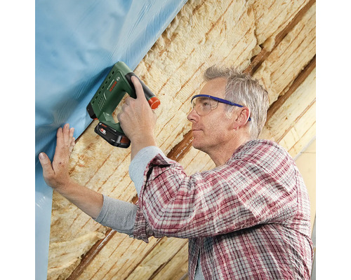 Ein Mann befestigt eine Folie mit einem Tacker an einer Dachkonstruktion.