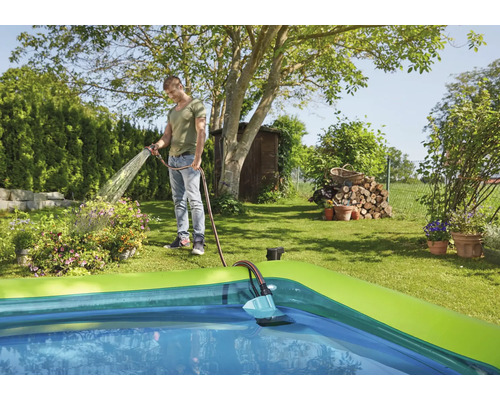 Mann bewässert Garten mit Schlauch neben Swimmingpool