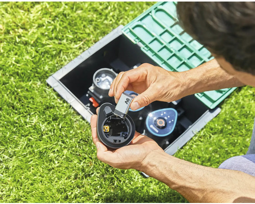 Person legt eine Batterie in einen Bewässerungscomputer im Garten
