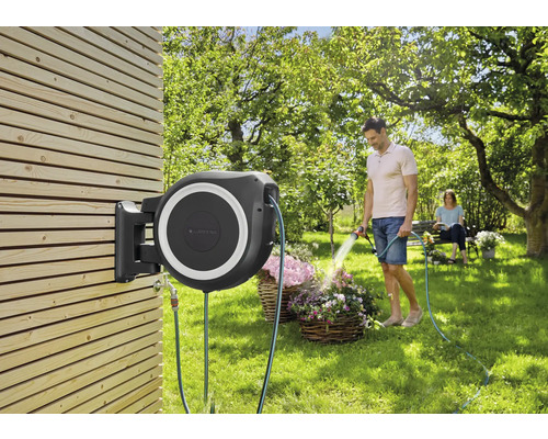 Boîtier de tuyau d''arrosage monté sur un mur en bois avec un homme arrosant des fleurs.