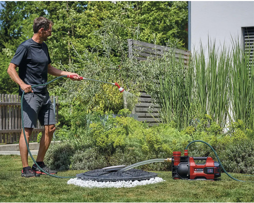 Mann bewässert Garten mit Gartenpumpe und Schlauch