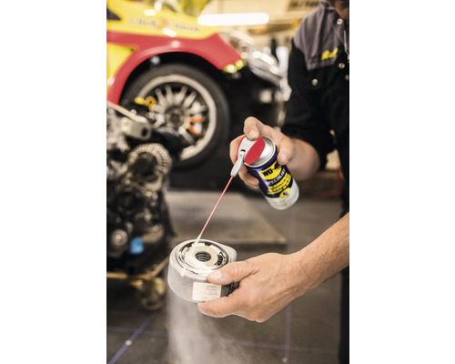 Eine Person sprüht WD-40 Specialist auf ein Metallteil vor dem Hintergrund eines Autos.