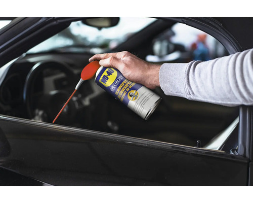 Eine Person sprüht WD-40 Silikonspray auf ein Autofenster.