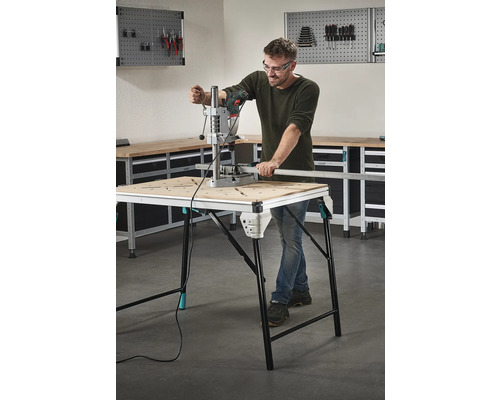 Mann arbeitet mit einer Bohrmaschine an einem Werktisch in einer Werkstatt.