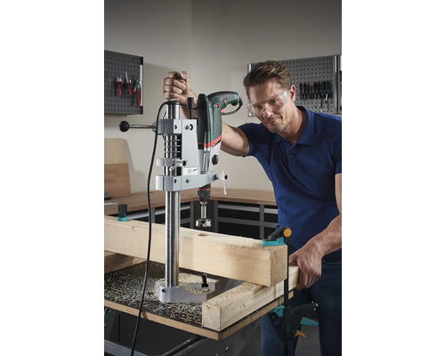 Mann bohrt mit Bohrmaschine und Bohrständer ein Loch in ein Holzstück.