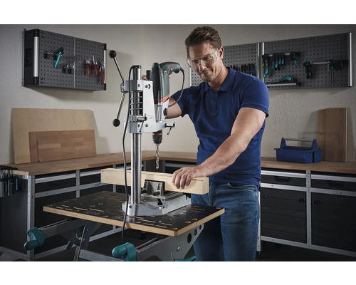 Mann arbeitet mit einer Tischbohrmaschine an einem Holzstück in einer Werkstatt