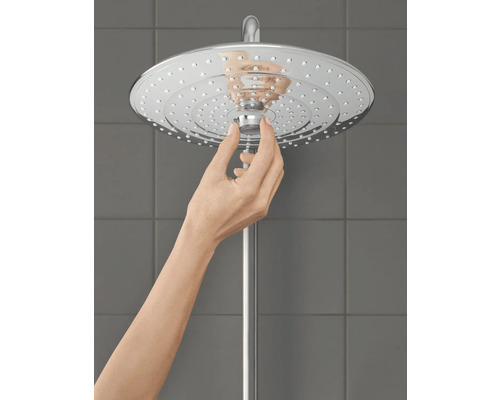 Une main ajuste une pomme de douche en métal.