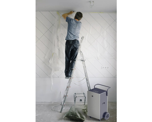 Mann auf einer Leiter, der eine Wand in einem Raum renoviert, mit einem Luftentfeuchter in der Nähe
