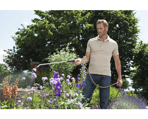 Un homme arrose des fleurs avec un pulvérisateur de jardin dans le jardin.
