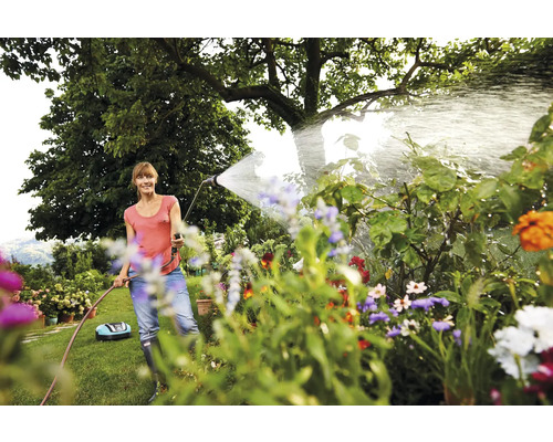 Femme arrosant des plantes dans le jardin avec un tuyau d''arrosage