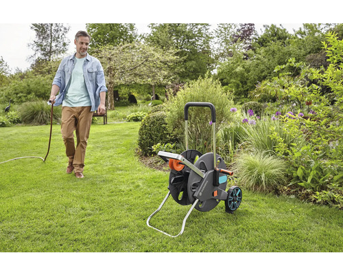 Mann zieht einen Gartenschlauch von einer Schlauchtrommel durch einen Garten