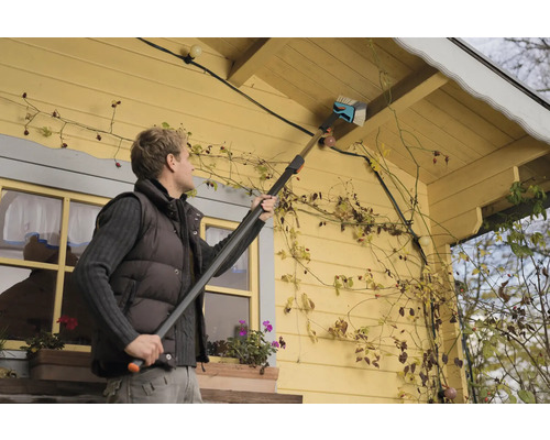 Une personne nettoie un toit de maison avec une brosse à gouttière.