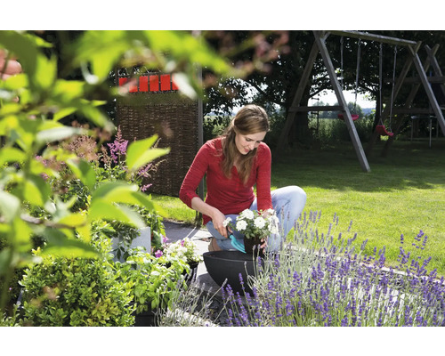 Une femme remplit un pot de fleurs dans le jardin.