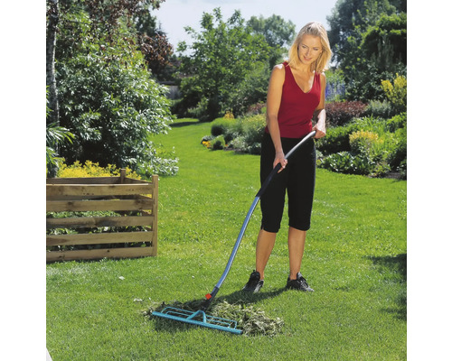 Une femme ratisse l''herbe avec un balai à gazon dans le jardin