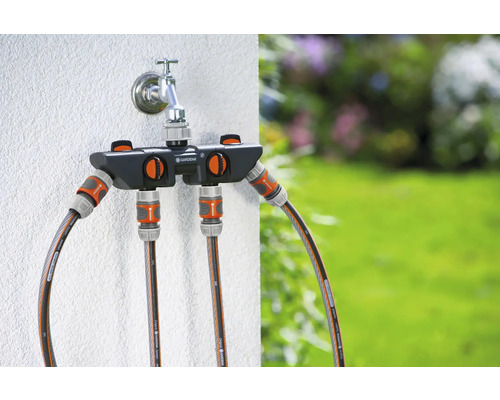 Robinet d''arrosage avec distributeur Gardena et tuyaux d''arrosage raccordés devant le jardin
