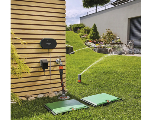 Scène de jardin avec système d''irrigation comprenant une unité de commande, un raccord de robinet et un arroseur oscillant escamotable