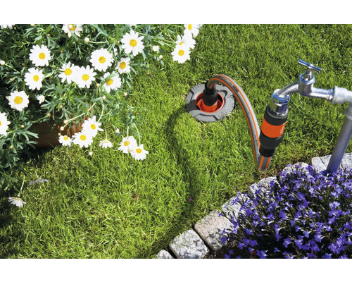 Gartenszene mit Wasserhahn, Gartenschlauch und Blumenbeet