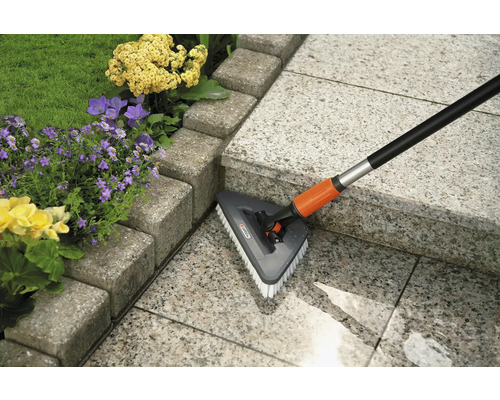 Brosse de nettoyage de terrasse avec manche télescopique en utilisation sur une terrasse en pierre à côté de fleurs