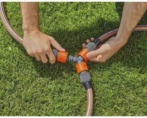 Person verbindet Gartenschlauch mit Verteilerstück auf Rasen
