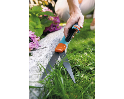 Personne coupant de l''herbe avec des cisailles à bordure de pelouse le long d''une pierre