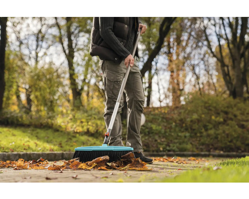 Une personne balaie les feuilles mortes avec un balai de rue à l''extérieur.