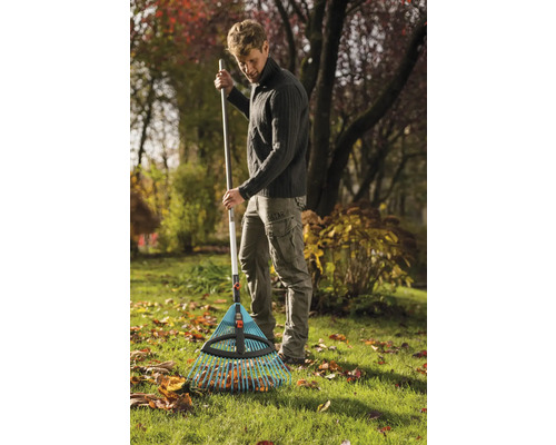 Un homme ratisse les feuilles mortes avec un râteau à feuilles dans le jardin.