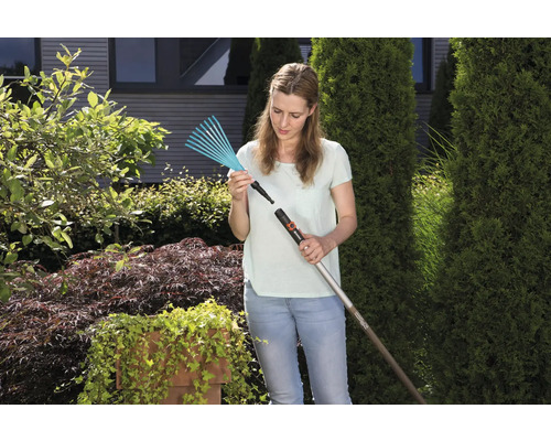 Une femme fixe une tête de râteau sur un manche dans le jardin.