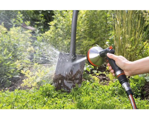 Eine Person reinigt eine schmutzige Schaufel mit einem Gardena-Sprühgerät im Garten.