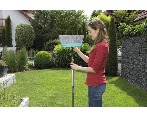 Femme utilisant un balai de voirie dans le jardin.